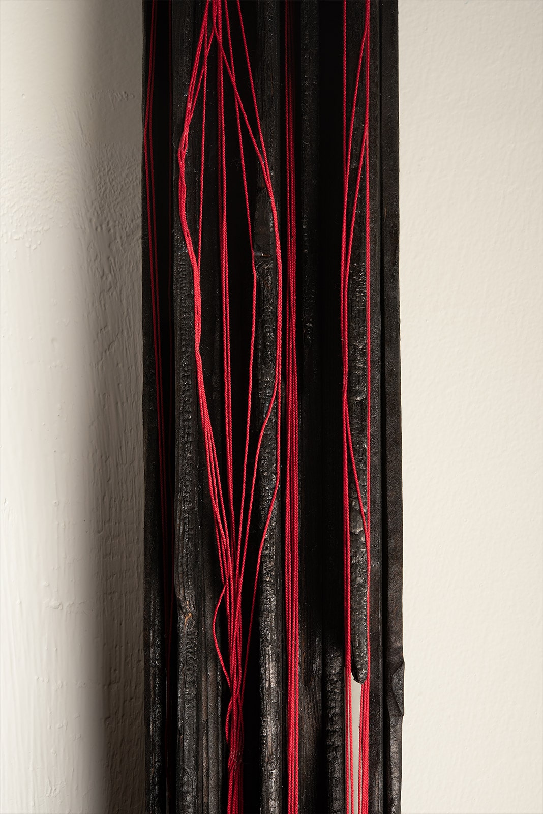 scultura di legno carbonizzato e fili di cotone rosso